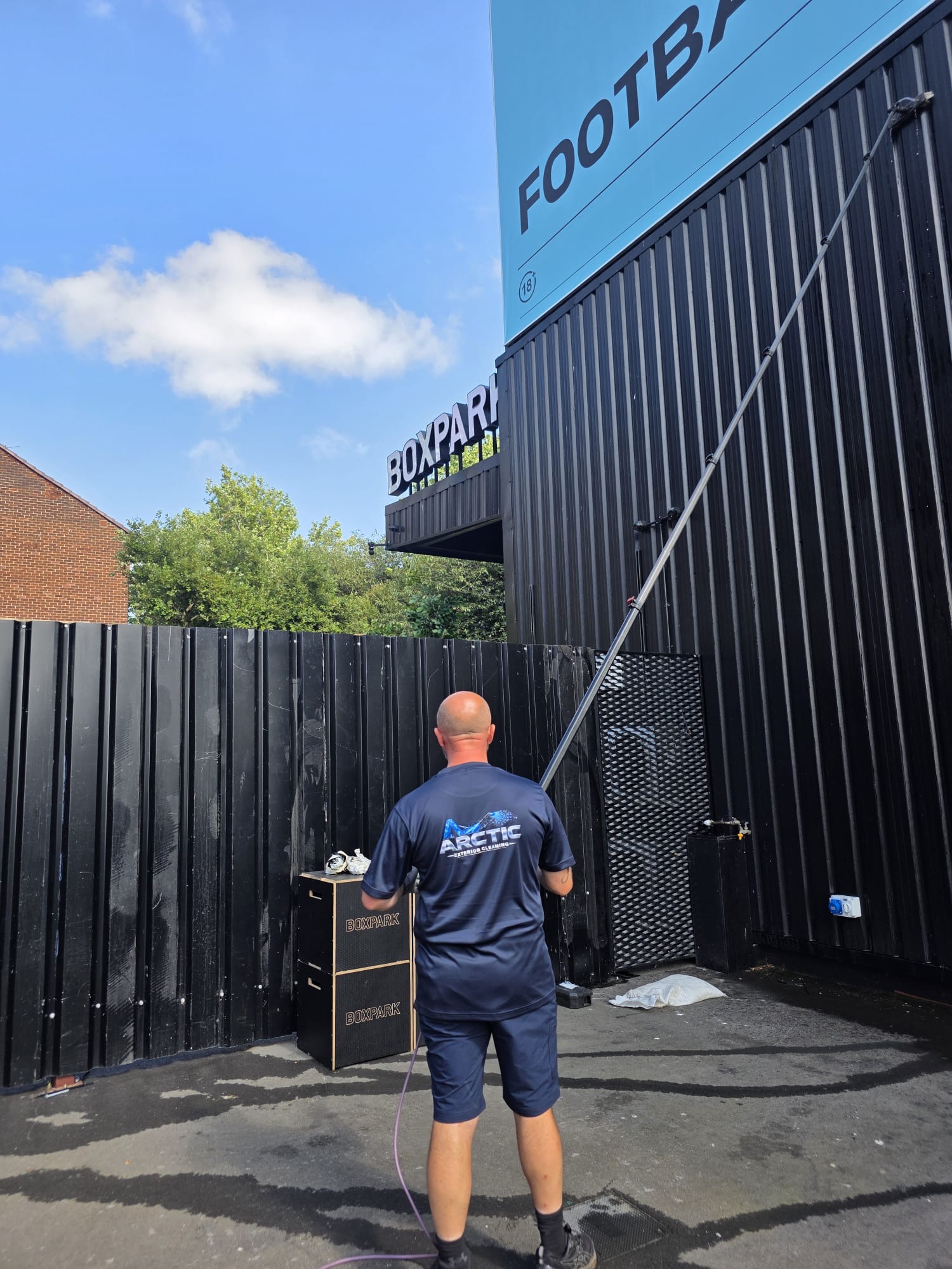 Arctic Exterior Cleaning technician soft washing a commercial façade with a long-reach pole