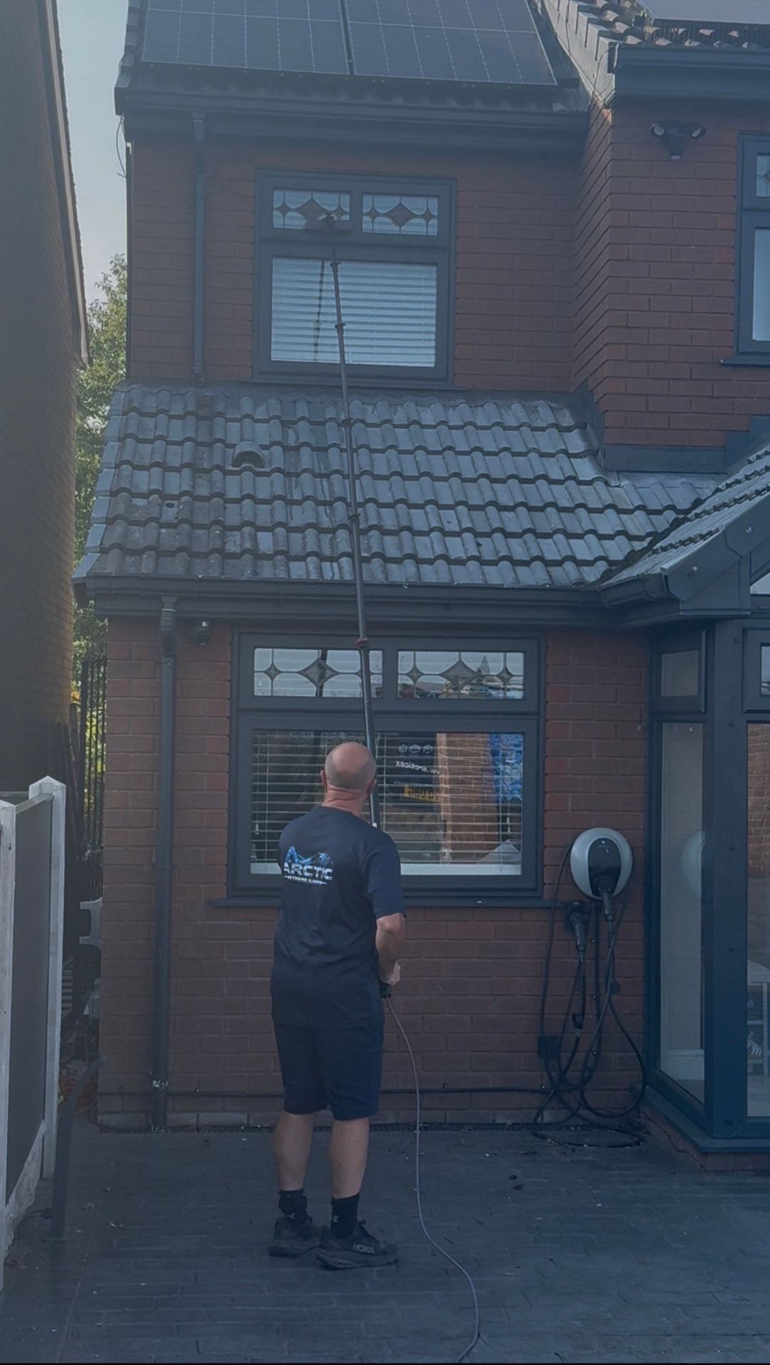 Arctic Exterior Cleaning technician cleaning upstairs windows of a house with a water-fed pole