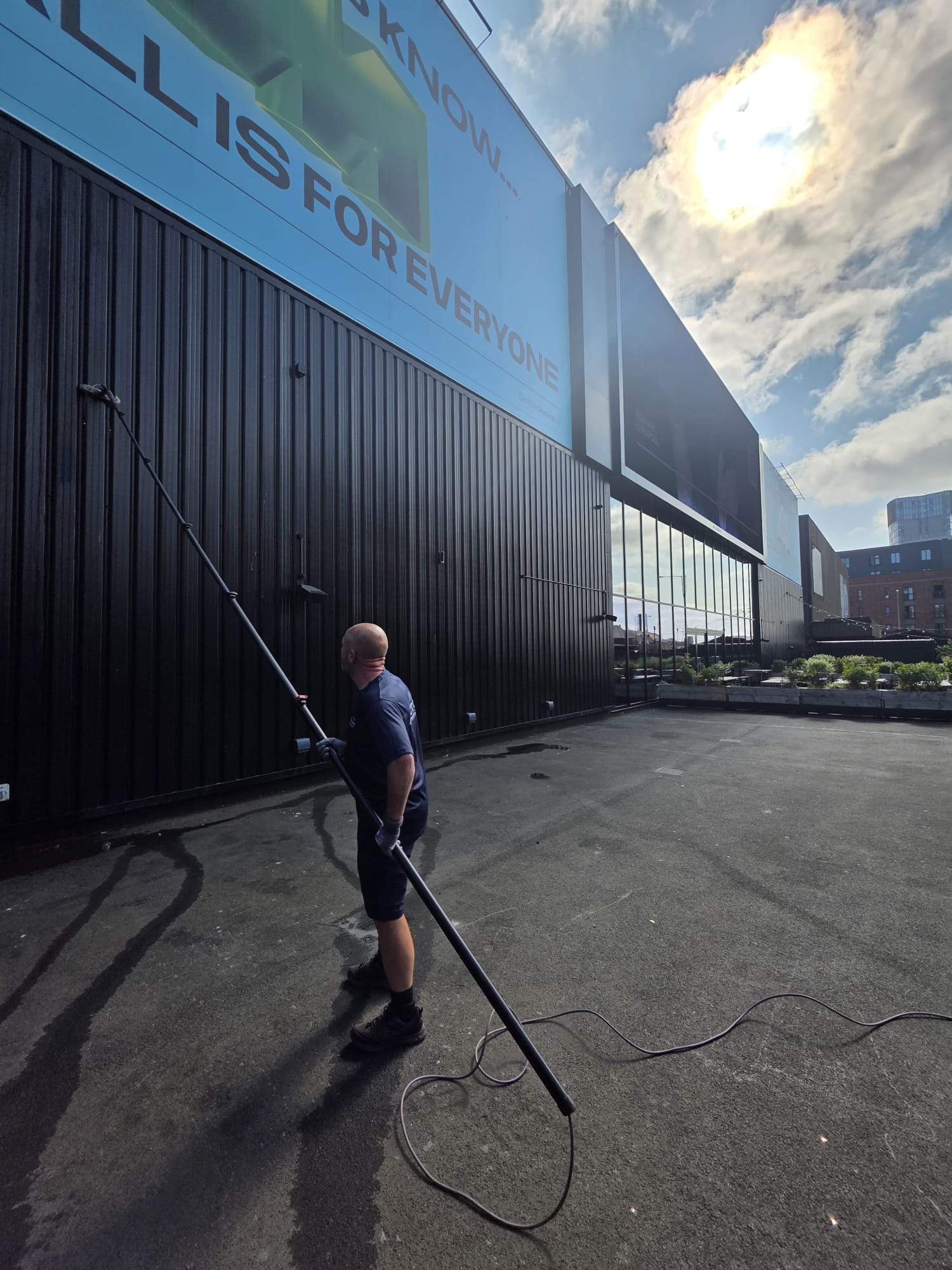 Arctic Exterior Cleaning technician using a water-fed pole to clean high-level cladding from a rooftop