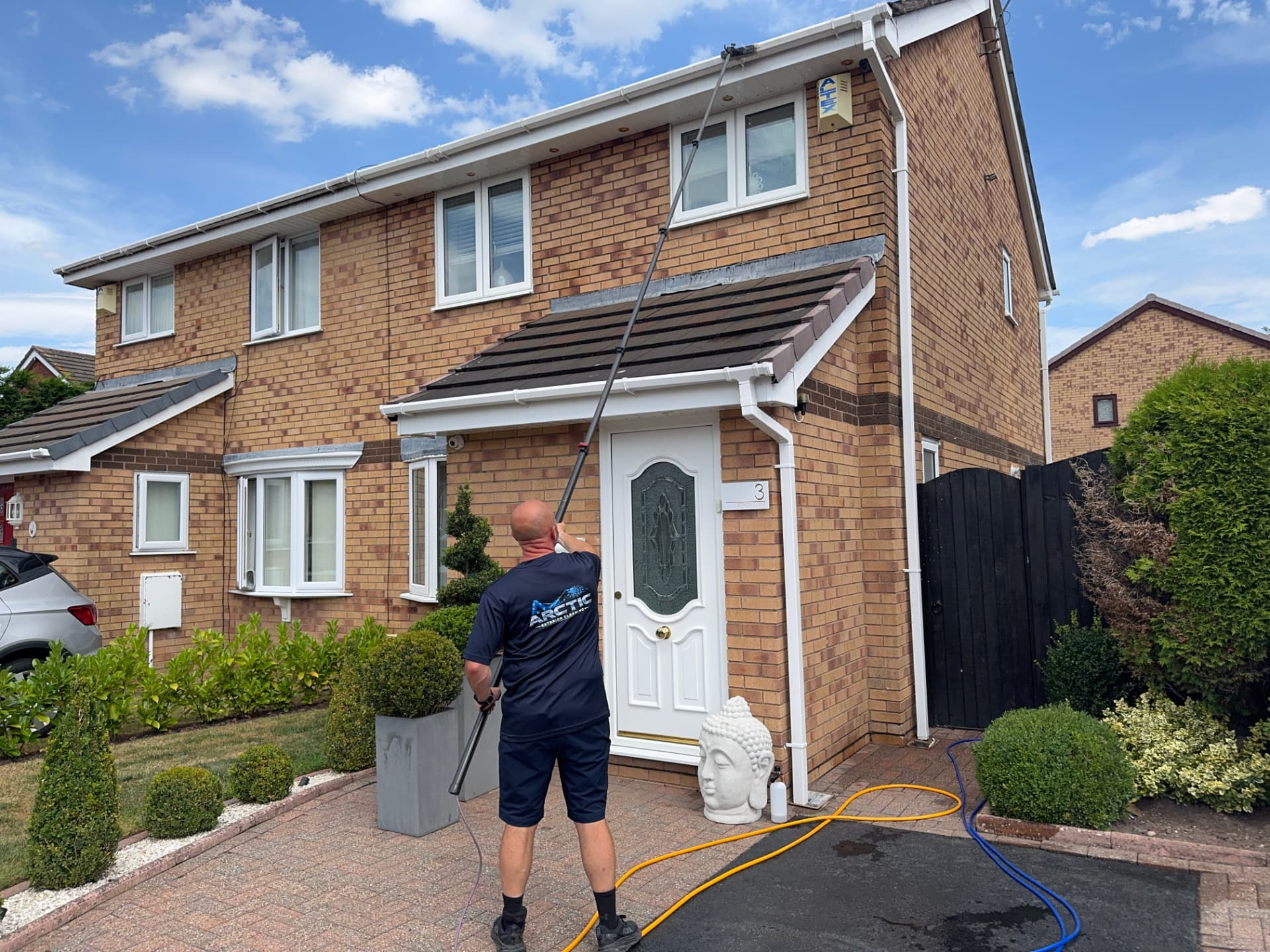 Arctic Exterior Cleaning technician clearing gutters and fascia from ground level with a long-reach pole