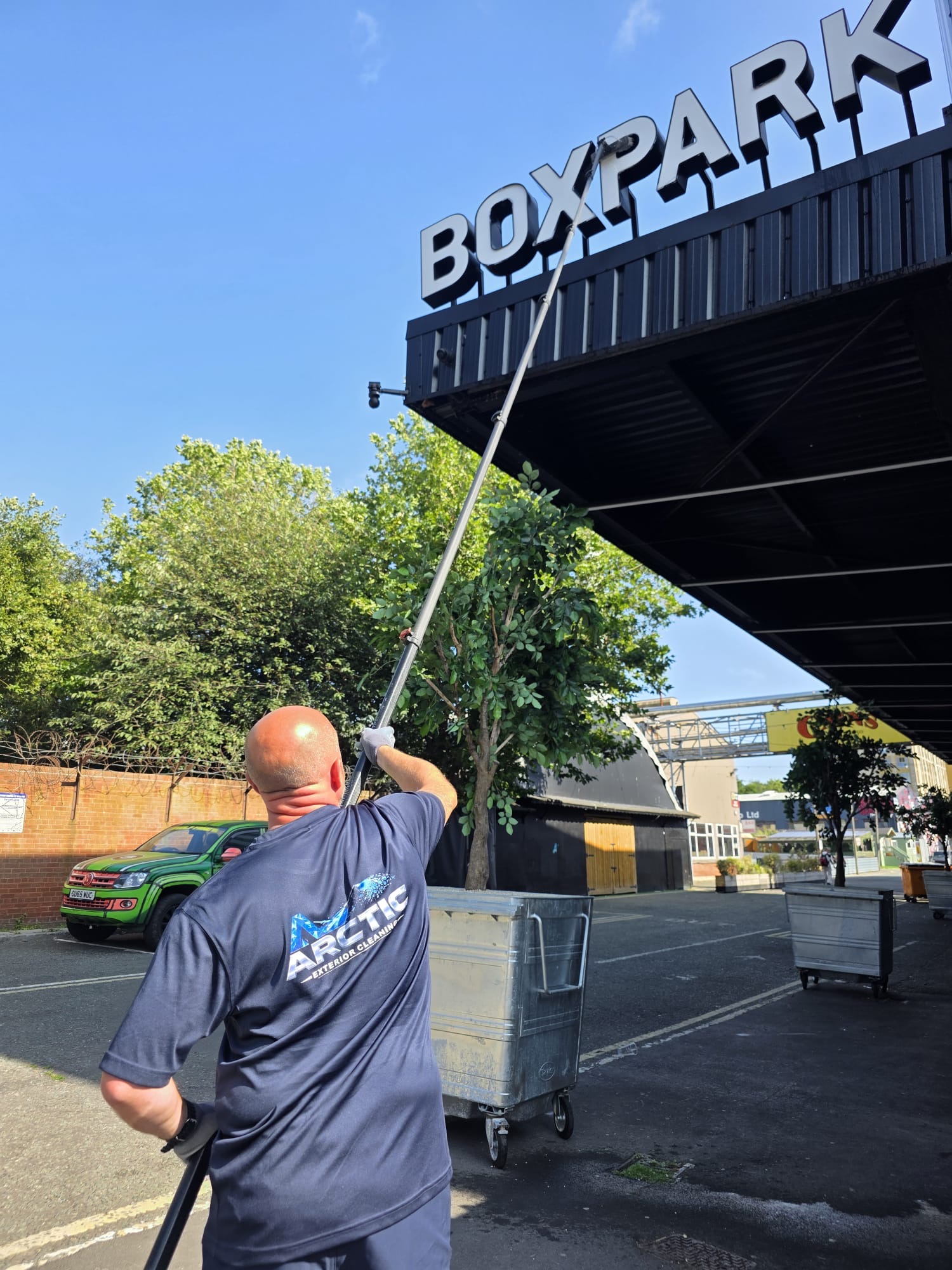 Arctic Exterior Cleaning technician cleaning building signage with a long-reach water-fed pole