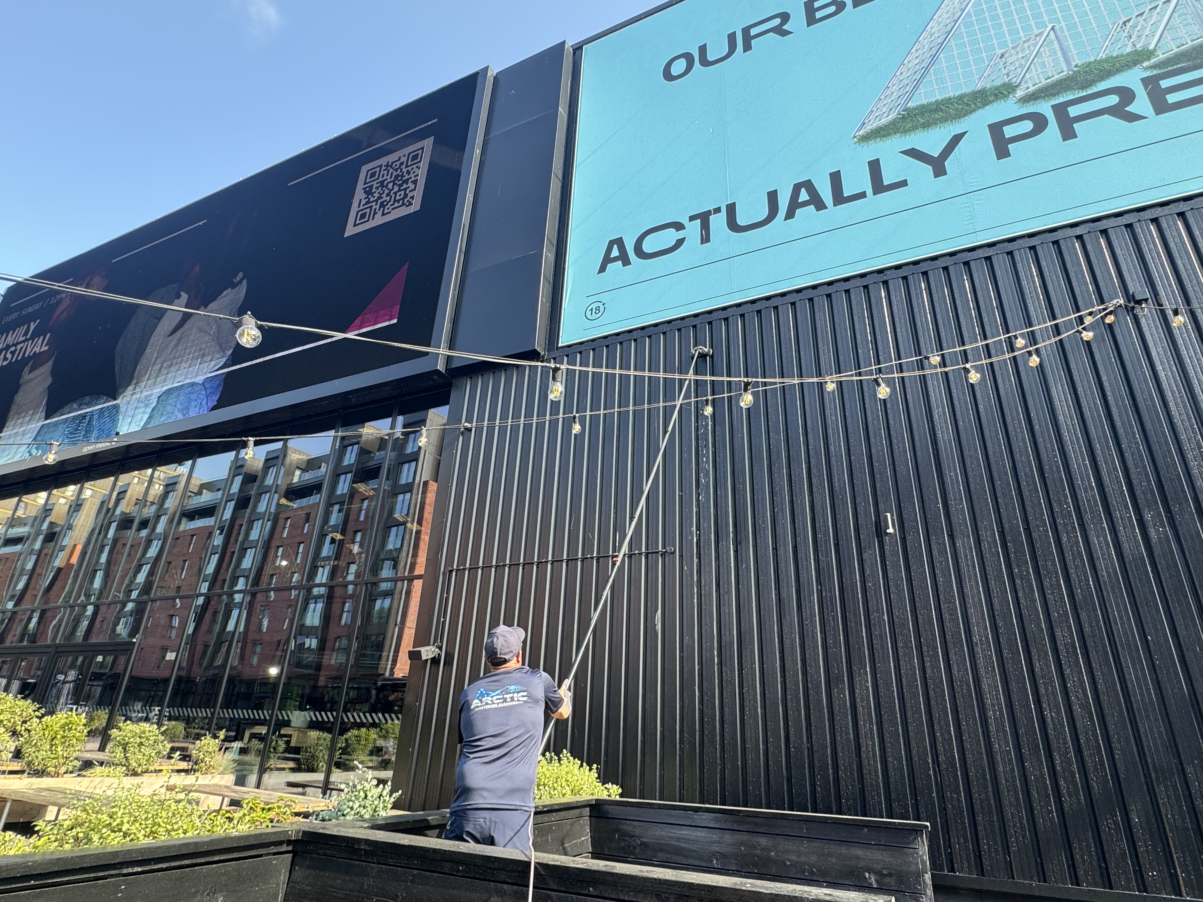 Arctic Exterior Cleaning technician cleaning black commercial cladding with a long-reach water-fed pole